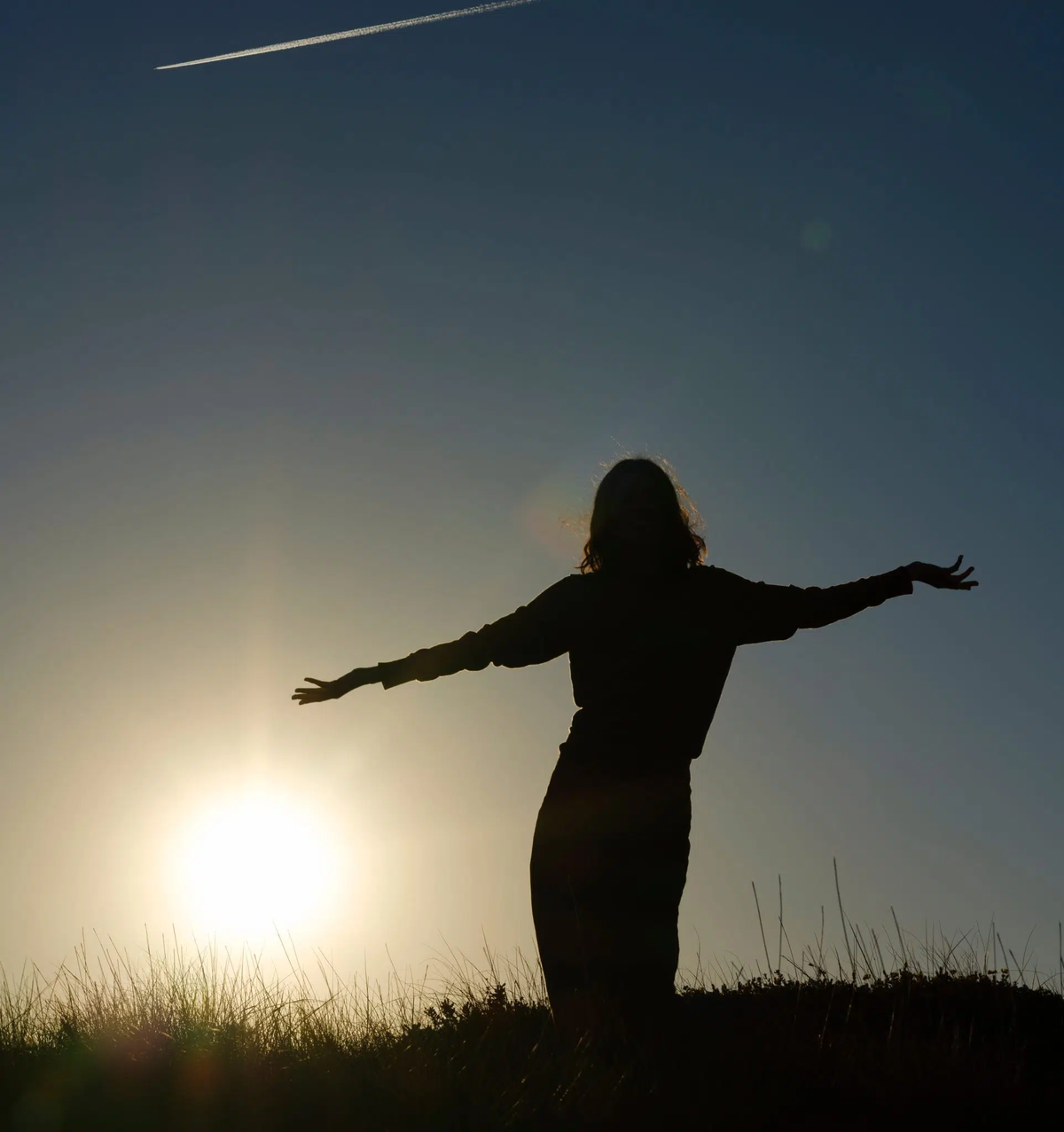 Frau tanz auf Wiese vor einem Sonnenuntergang